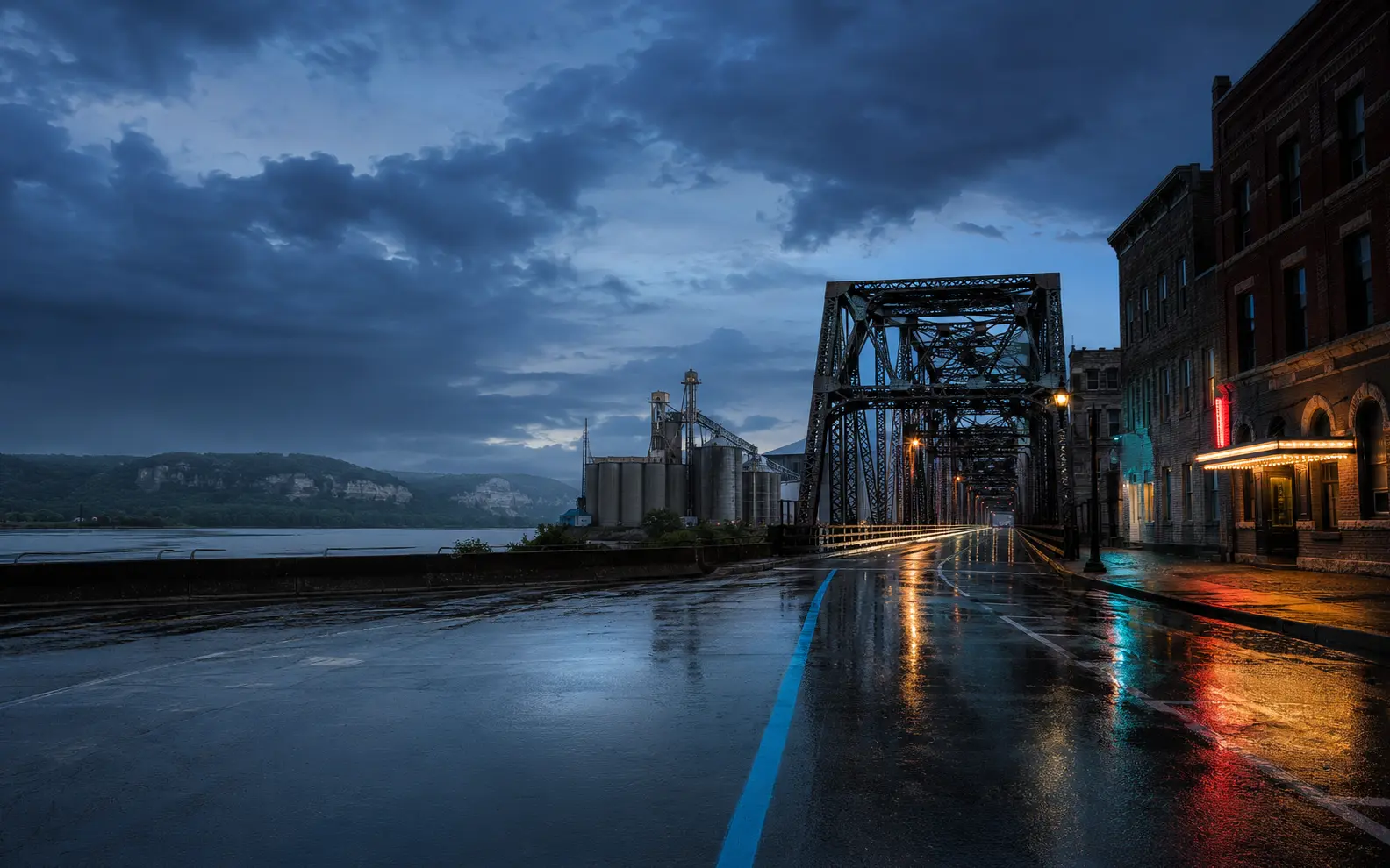 Conceptual blue-hour Illinois scene with a rain-wet road, steel bridge, river industry, and brick storefronts